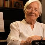 Delfina Guzmán junto a un piano, una partitura y su libro de memorias