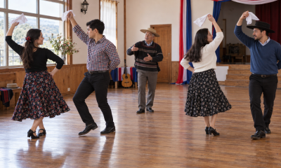 Dos parejas practican cueca mientras un instructor guía los pasos en un salón comunitario