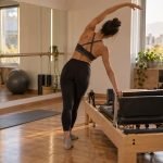 Joven practica movimiento corporal junto a una máquina Pilates Reformer en un estudio luminoso