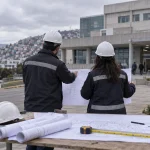 Profesionales revisan planos de infraestructura frente a un hospital en una imagen editorial referencial