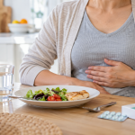 Persona con molestia en la parte alta del abdomen frente a una comida ligera y agua