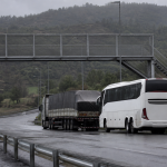 Bus interurbano y camión detenidos junto a una pasarela en una autopista húmeda
