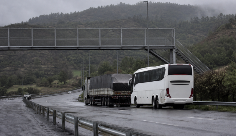 Bus interurbano y camión detenidos junto a una pasarela en una autopista húmeda