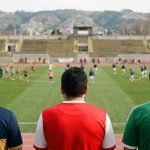 Tres hinchas con colores de clubes de la Región de Valparaíso observan una cancha antes de los partidos del fin de semana