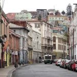 Calle urbana de Valparaíso con edificios, vehículos estacionados y un bus