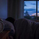 Reloj despertador junto a una persona que duerme antes del amanecer