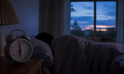 Reloj despertador junto a una persona que duerme antes del amanecer