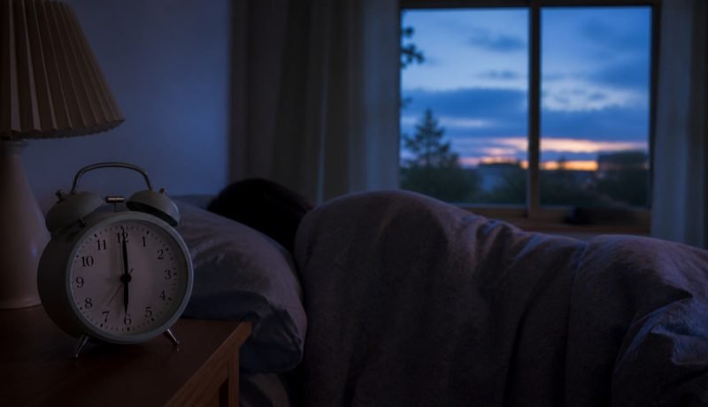 Reloj despertador junto a una persona que duerme antes del amanecer