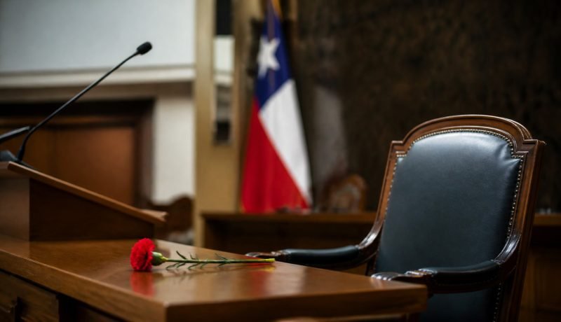Atril y asiento vacíos con una bandera chilena y un clavel rojo