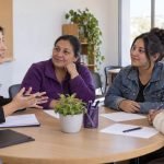 Representación editorial de una orientadora conversando con tres mujeres en una mesa comunitaria