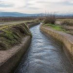 Canal de riego rural en un paisaje agrícola después de lluvias de invierno