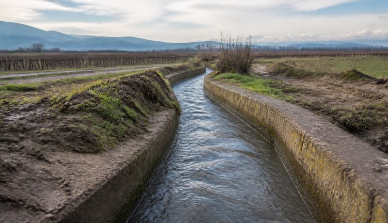Canal de riego rural en un paisaje agrícola después de lluvias de invierno