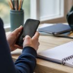 Estudiante usa un teléfono junto a cuadernos escolares