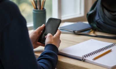 Estudiante usa un teléfono junto a cuadernos escolares