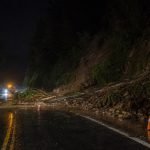 Derrumbe de tierra y árboles bloquea una carretera rural mojada durante la noche