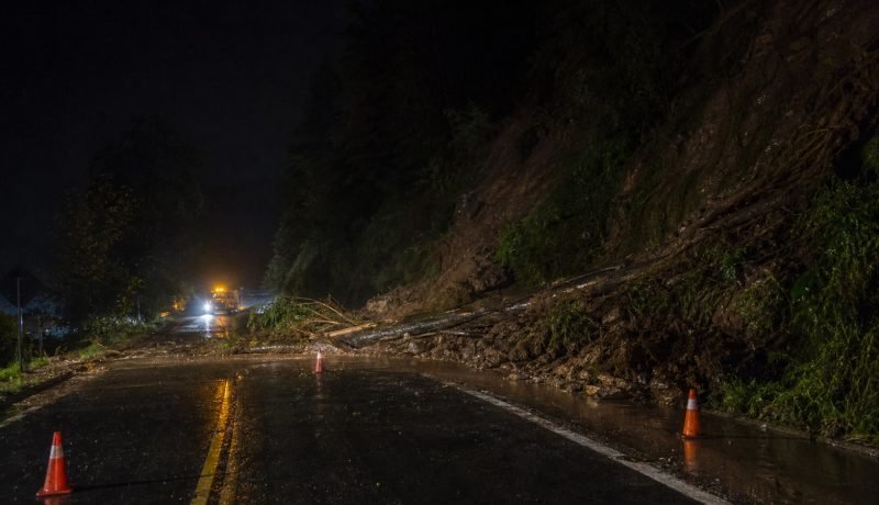 Derrumbe de tierra y árboles bloquea una carretera rural mojada durante la noche