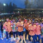 Músicos sobre un escenario ante un público numeroso en una celebración al aire libre.