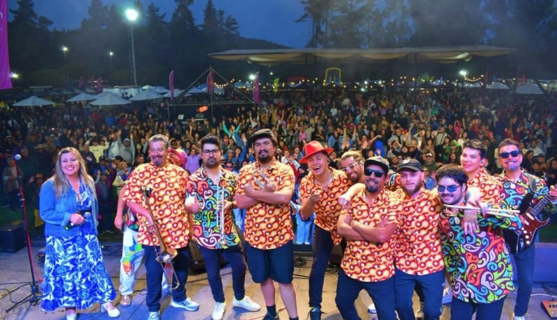 Músicos sobre un escenario ante un público numeroso en una celebración al aire libre.