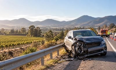 Vehículo con daños frontales detenido junto a una carretera, con equipos de emergencia al fondo