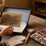 Manos revisan una fotografía antigua junto a objetos patrimoniales