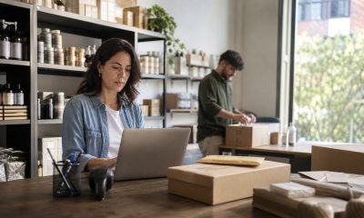 Propietaria de una pequeña empresa revisa ventas mientras un trabajador prepara despachos