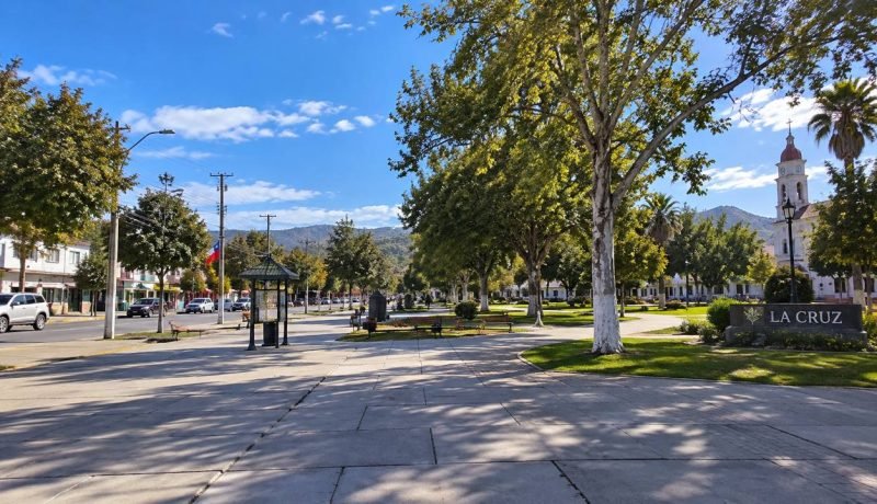Plaza arbolada de La Cruz, con senderos, bancos y una iglesia al fondo.
