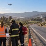Equipo de emergencia revisa un mapa junto a una ruta rural con un dron en vuelo