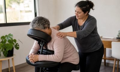 Persona mayor recibe un masaje de hombros en una sala comunitaria