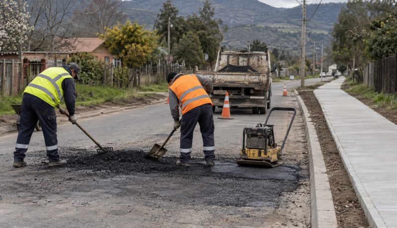 Trabajadores realizan bacheo en una calle comunal junto a una acera nueva