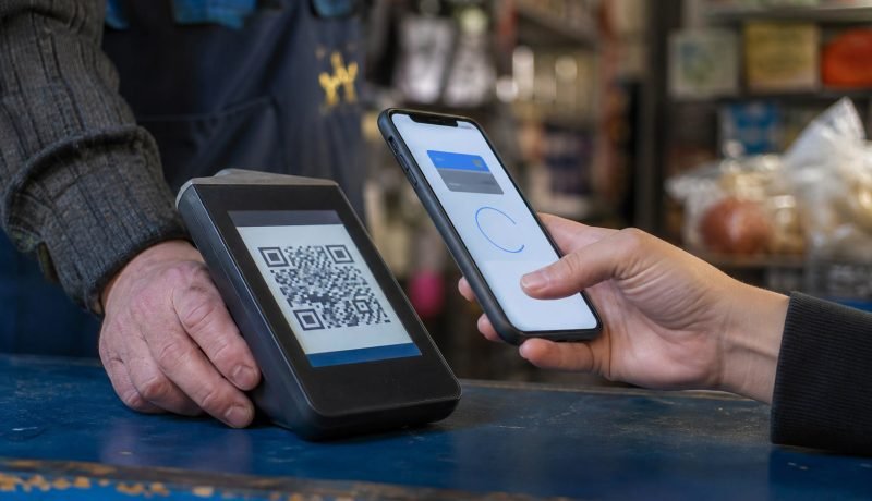 Persona acerca su teléfono a un código QR en el terminal de un comercio