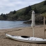 Kayak, quitasol plegado y estructura de madera en una playa de la costa central