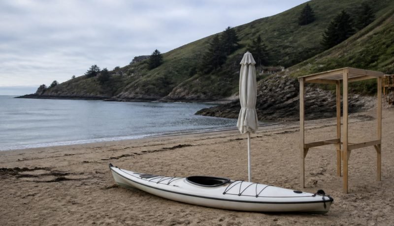 Kayak, quitasol plegado y estructura de madera en una playa de la costa central