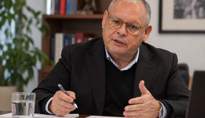 Hombre con anteojos sentado ante documentos y un cuaderno en una oficina