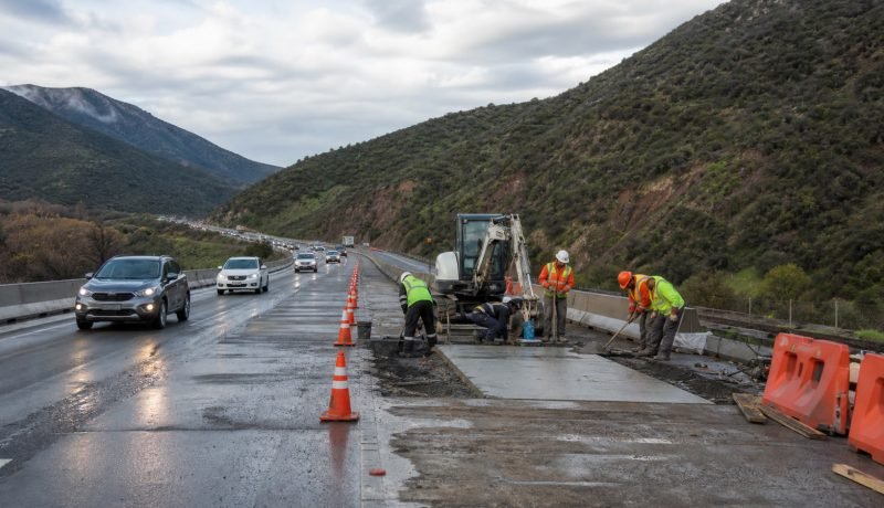Trabajadores realizan obras de hormigón en una pista de autopista con tránsito habilitado al costado