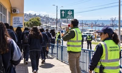 Estudiantes caminan hacia una zona de seguridad acompañados por personal de prevención y emergencias.