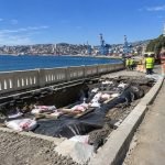 Socavón junto a una vía costera, con obras, conos y una señal de precaución.