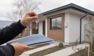 Manos con llaves y documentos frente a una vivienda nueva