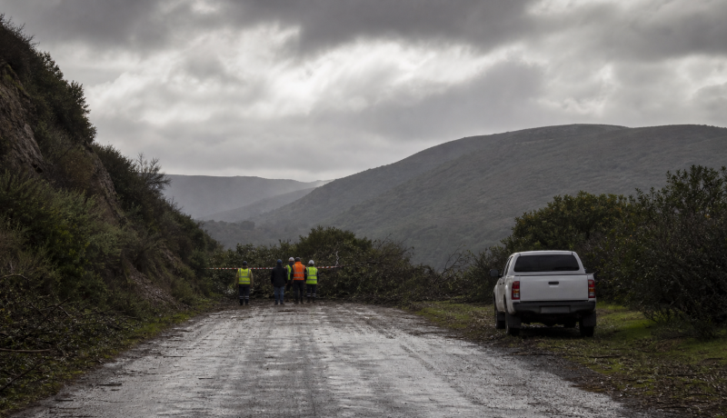 Camino rural húmedo con personal de emergencia visto a distancia tras un sistema frontal, imagen editorial referencial